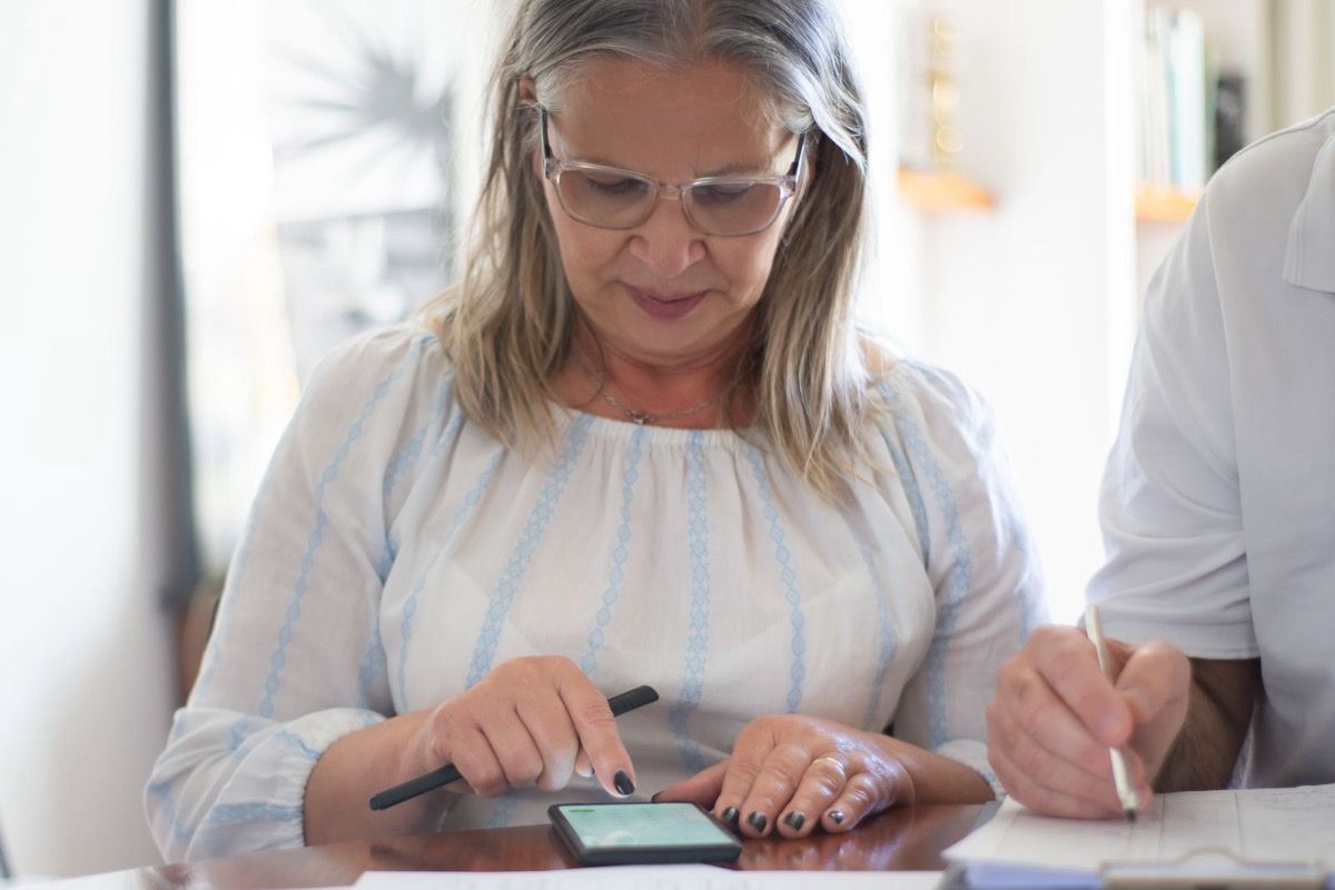 Woman over 50 reviewing a smartphone and paperwork with another person