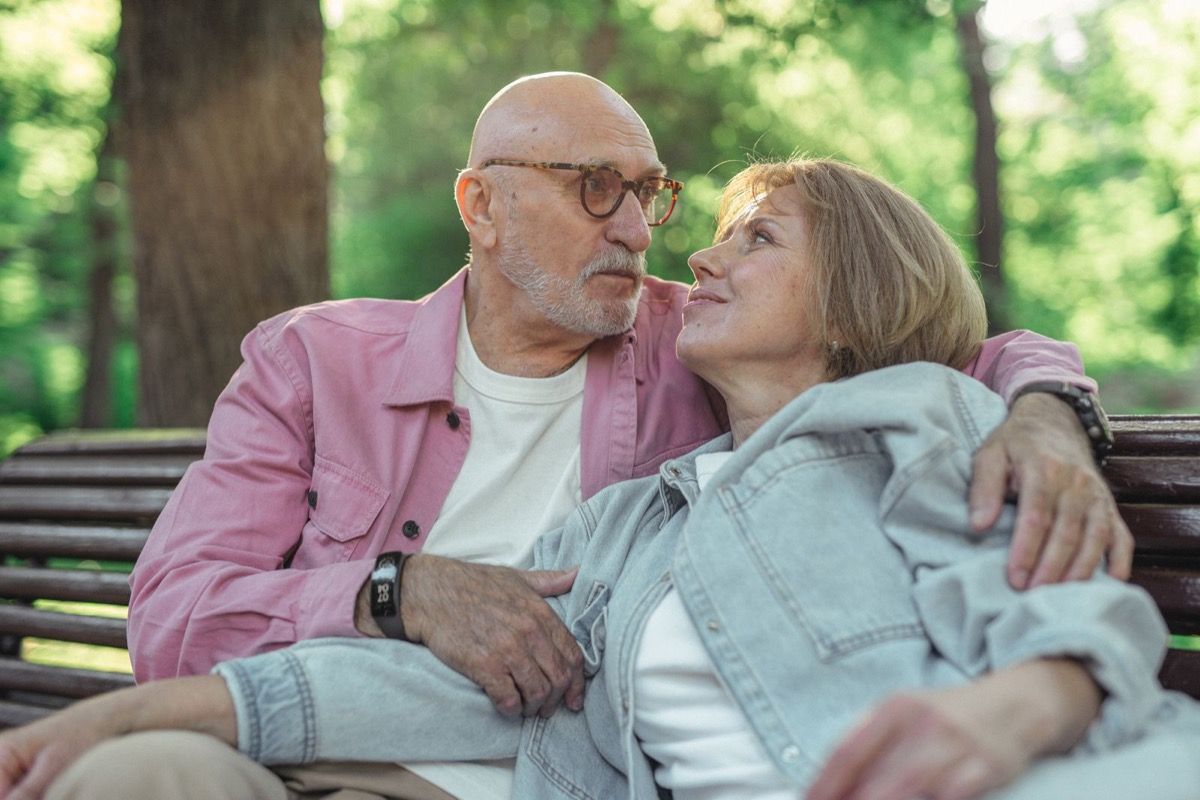 A couple with a visible age difference sharing a warm moment together on a park bench