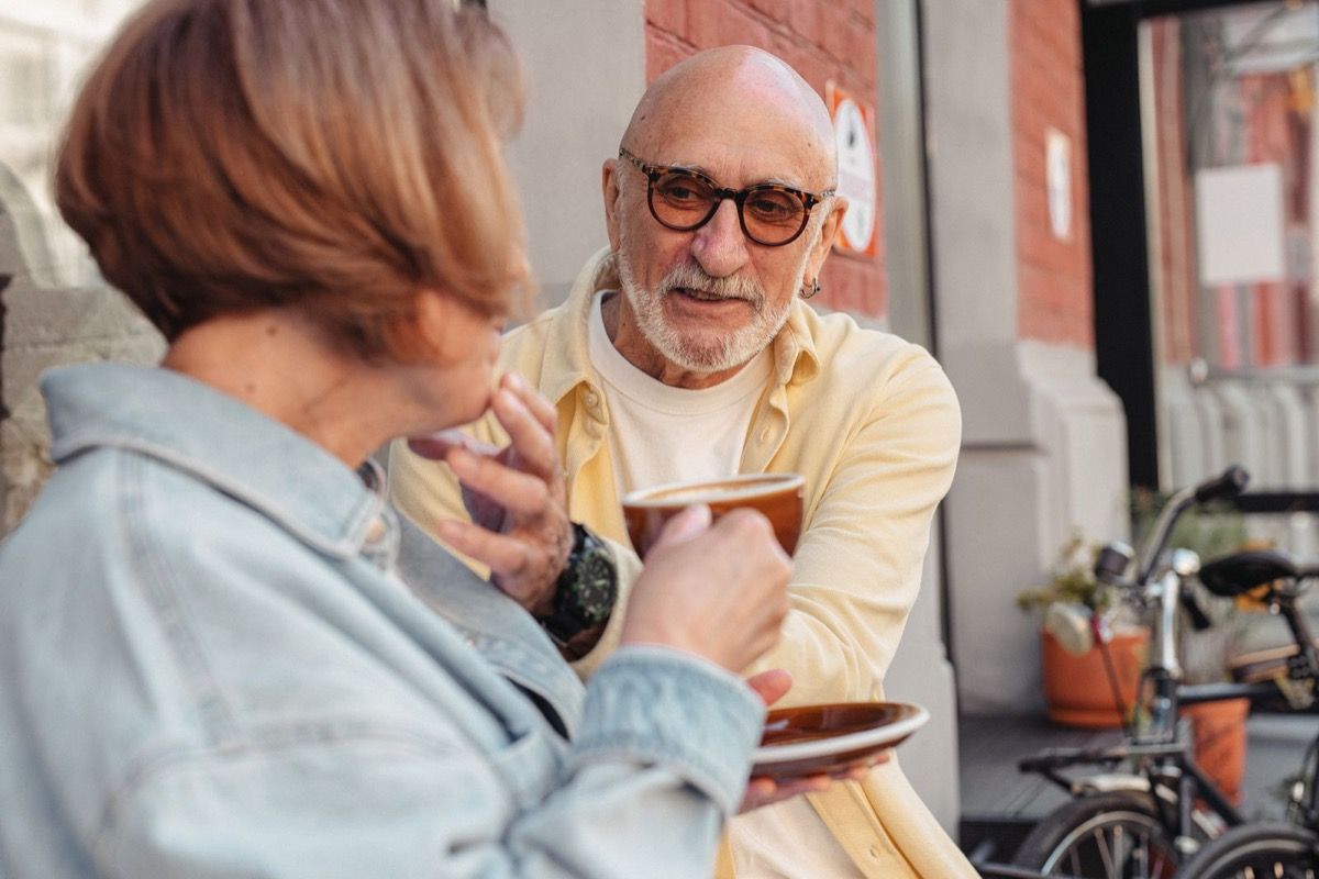 Two adults over 50 having coffee together at a cafe, engaged in relaxed conversation during the daytime