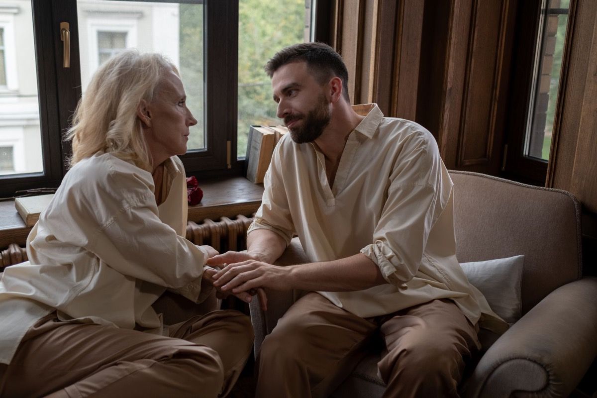 A woman over 50 and a younger man sharing a relaxed conversation on a couch by a window