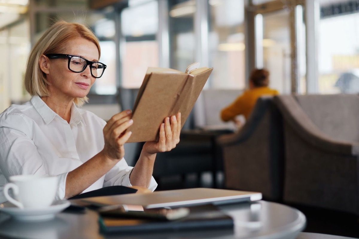 Woman over 50 sitting at a cafe with a book and coffee, relaxed and self-assured