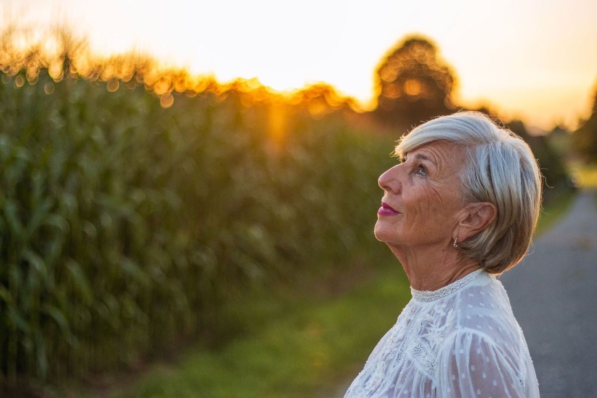 Woman with silver hair looking upward in warm sunset light on a quiet rural path