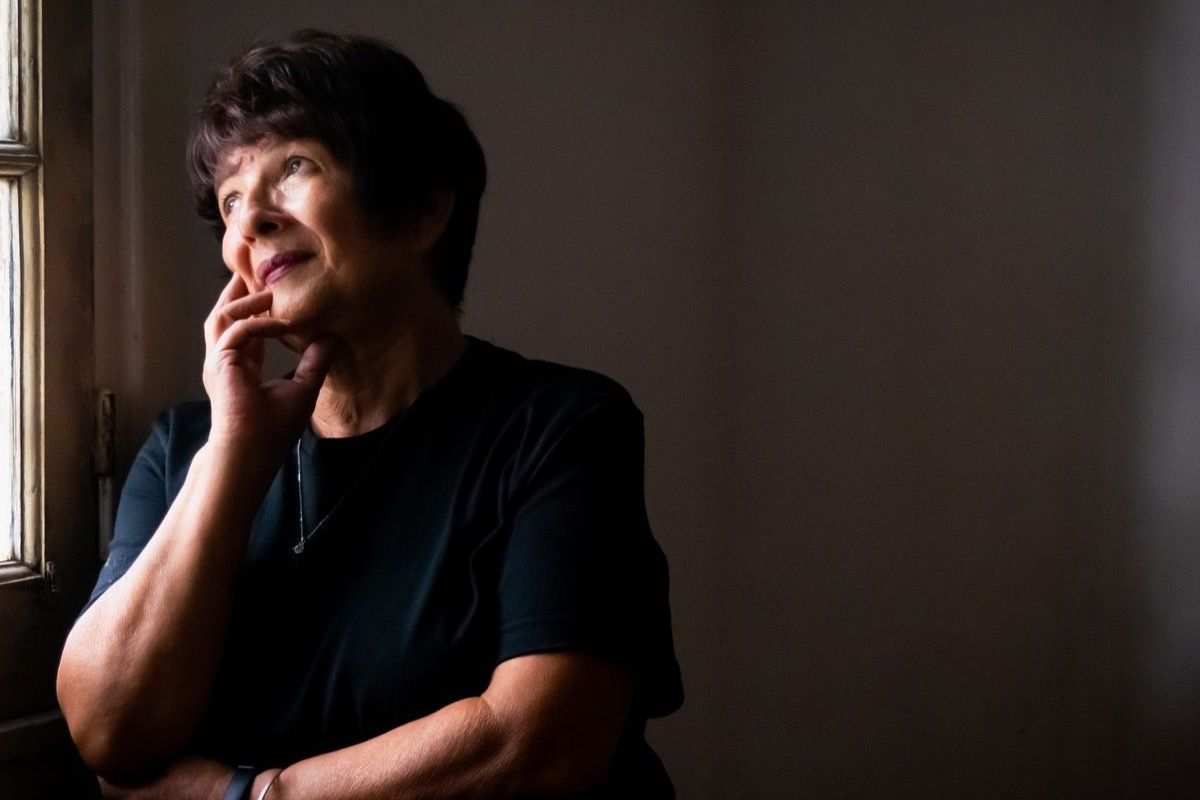 Woman over 60 gazing pensively through a window in soft natural light, contemplative and calm