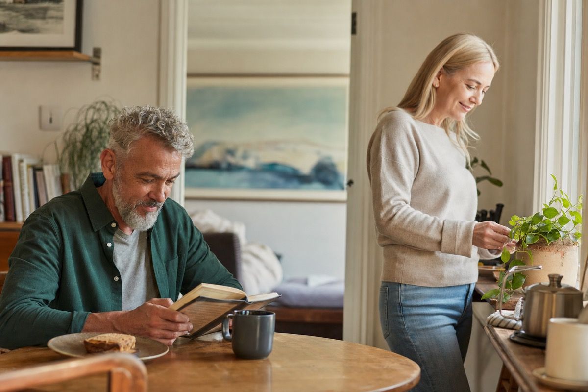 Two adults over 50 sharing a calm home moment while each keeps their own activity