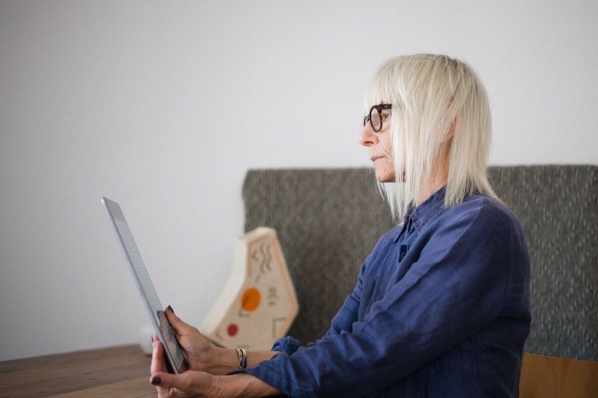 Woman over 60 with glasses carefully reading a tablet at home, evaluating what she has just read