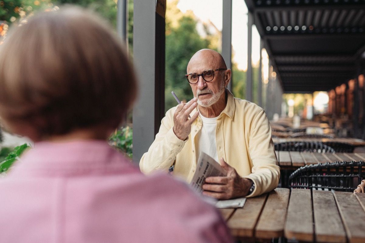 Man over 50 speaking with a woman across an outdoor cafe table